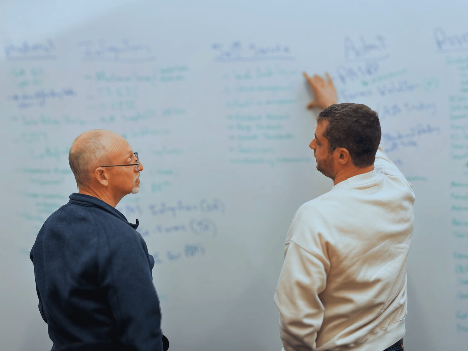 One man explaining a concept to another at a whiteboard